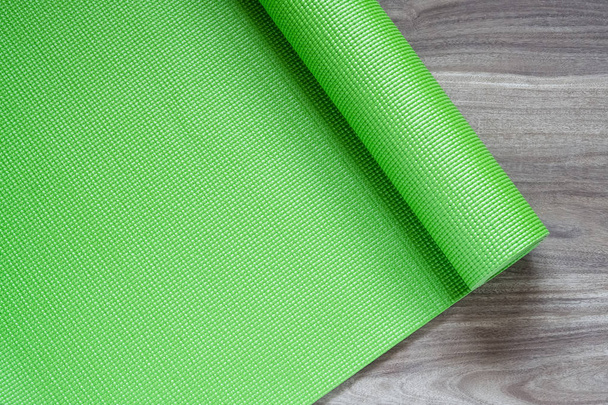 Зеленый коврик для йоги на деревянном фоне, вид сверху с копировальным пространством. Концепция здорового образа жизни
. - Фото, изображение