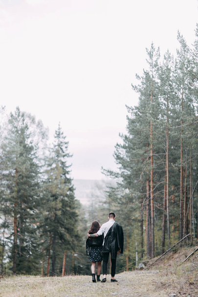 Young stylish couple in the forest, running around the Park and laughing. Modern people on a walk. Beautiful girl with tattoos. Loving young man and girl. mountain Park with pine forest - Foto, Imagem