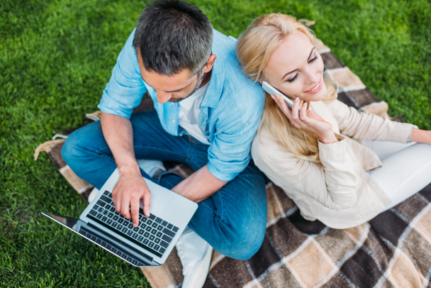 high angle view of happy couple using smartphone and laptop in park  - Photo, Image