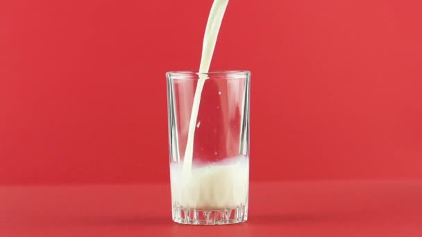 Slow motion close-up shot of cold diary milk cold beverage drink pooring into threaded glass red background in studio - Footage, Video