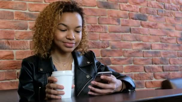 Nowoczesny piękny African-American dziewczyna trzyma kubek biały i telefon i mówi coś takiego. Strzelać wideo z rąk. - Materiał filmowy, wideo