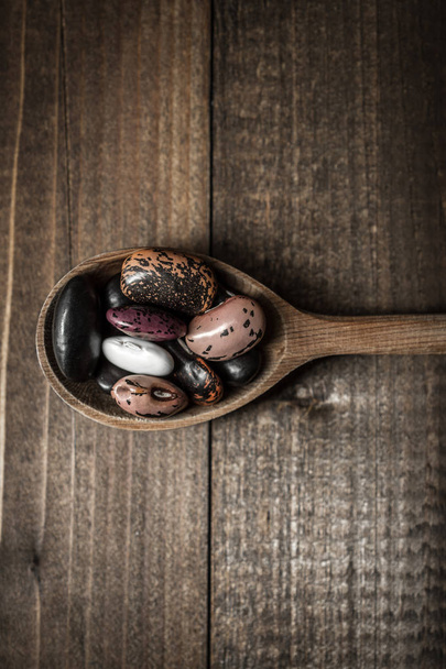 Haricots colorés crus et cuillère en bois sur fond sombre
 - Photo, image