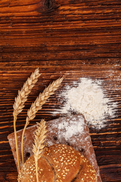 Celozrnné pšeničné pečivo s moukou a hroty na dřevěný stůl z výšky. - Fotografie, Obrázek