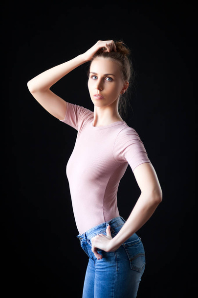 Porträt einer attraktiven jungen Frau in beigem Top und Jeans, die vor schwarzem Hintergrund posiert. - Foto, Bild