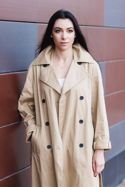 Женщина в бежевом пальто на улице, мягкий фокус на фоне
 - Фото, изображение