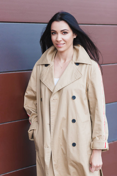Beautiful woman in the beige coat on the street, soft focus background - Фото, изображение