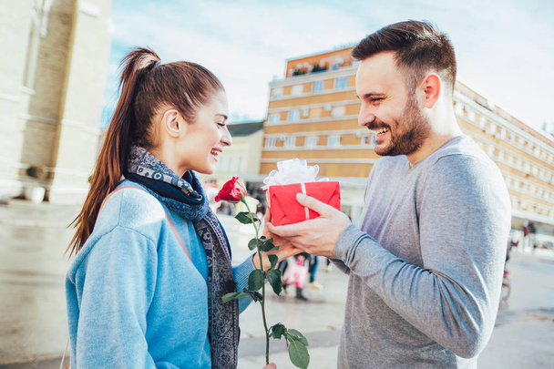 Мужчина удивляет женщину подарком и розой в городе
 - Фото, изображение