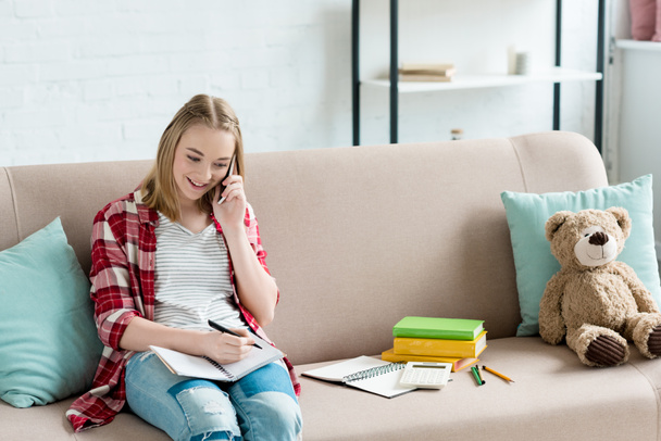 teen student girl doing homework on couch and talking by phone - Fotografie, Obrázek