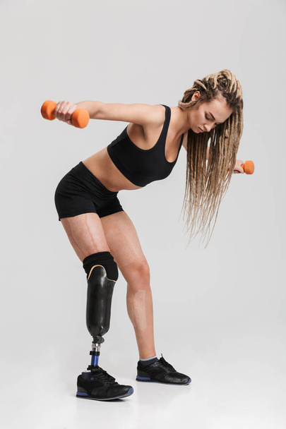 Image of a healthy young disabled sportswoman standing isolated over grey background make exercises with dumbbells. - Foto, imagen