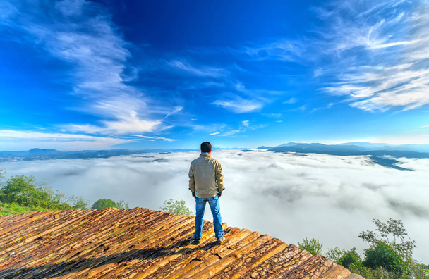 Silueta mladý muž stojí na vysokém kopci malebné venkovské město v ranní mlze údolí zahalené hory a velké zvlněné malebné místo pro nativní Vietnam - Fotografie, Obrázek