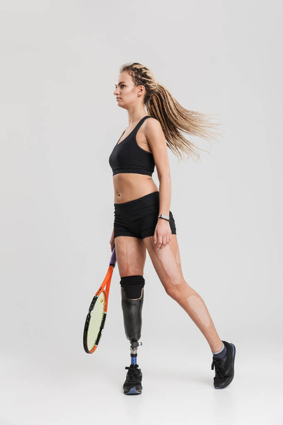 Picture of a gorgeous young disabled sportswoman tennis player standing isolated over grey background play tennis. - 写真・画像