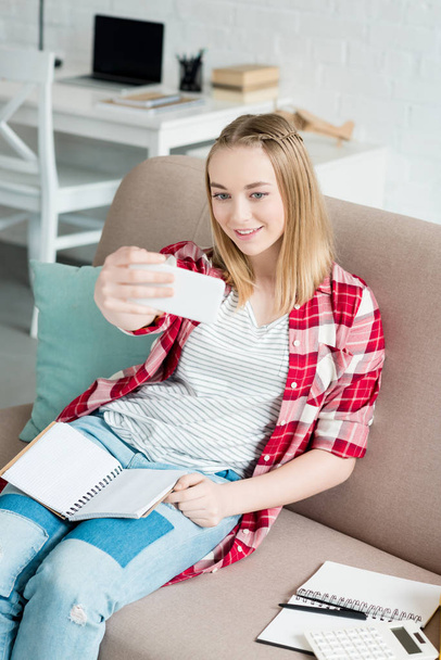 teen student girl with notebook sitting on couch and taking selfie - Foto, Bild