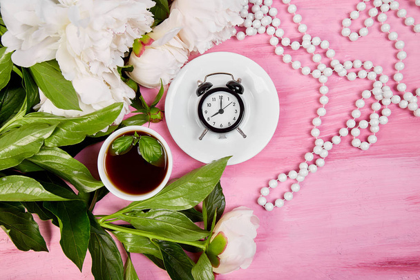 おはようございます。紅茶、目覚まし時計、ピンク色の背景に白の牡丹の花束。フラットが横たわっていた。平面図です。コピー スペース. - 写真・画像