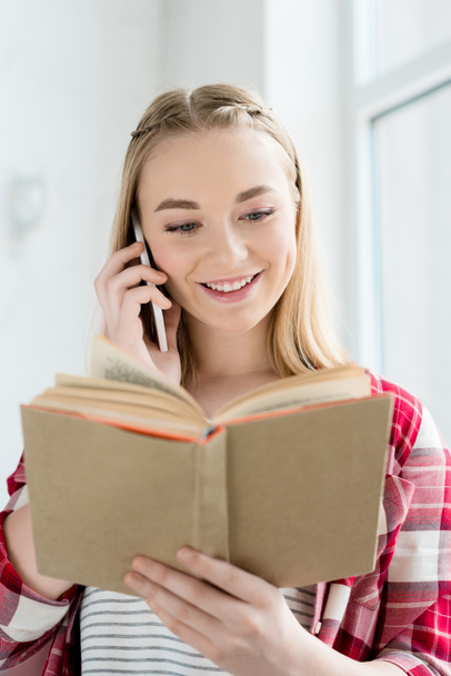 close-up portrait of happy teen student girl reading book and talking by phone - Foto, afbeelding