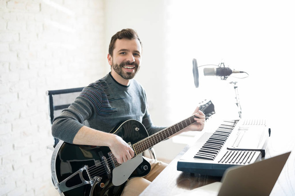 Jeune homme souriant assis à la station de radio avec guitare faisant un contact visuel
 - Photo, image