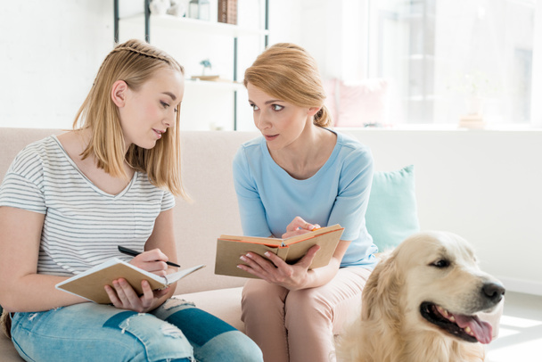 mother and teen daughter doing homework together while their golden retriever sitting on floor - Foto, immagini