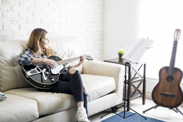 Schattig vrouwelijke musicus gitaarspelen thuis en glimlachen - Foto, afbeelding