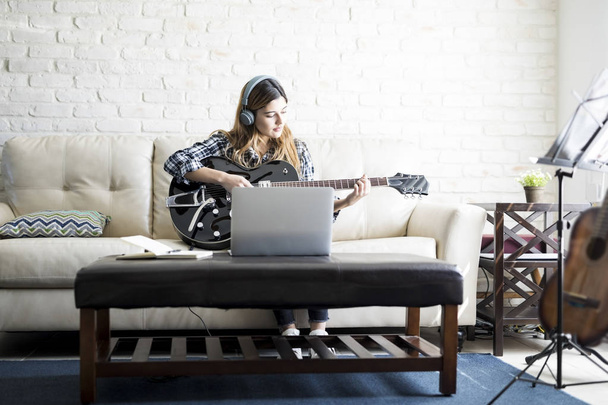 Creative young caucasian woman with guitar composing a new song and recording it into her laptop - Фото, изображение