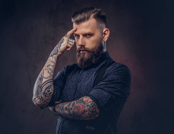 Pensive old-fashioned hipster in a blue shirt and suspenders, standing in a studio. - Foto, Imagem