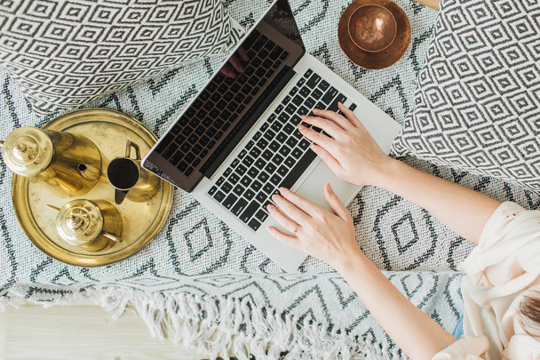 Young woman working on laptop in bed. Lifestyle top view, flatlay composition in boho interior design. Freelancer or fashion blogger home workspace concept. - Foto, imagen
