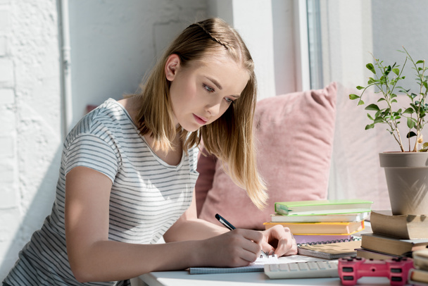 centrado adolescente estudiante chica haciendo tarea en windowsill
 - Foto, Imagen