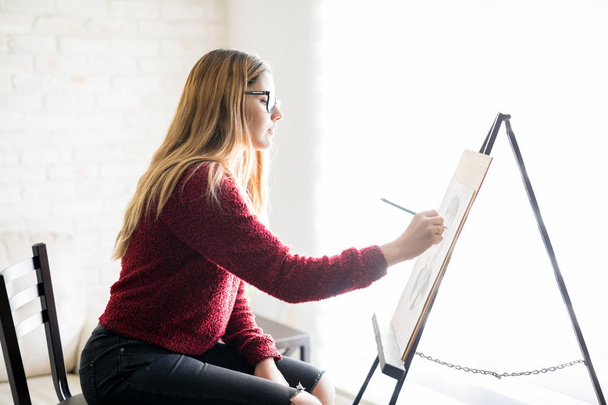 Το προφίλ άποψη του χαριτωμένο νεαρή γυναίκα ζωγράφος κάνει κάποια ζωγραφική σε καμβά - Φωτογραφία, εικόνα