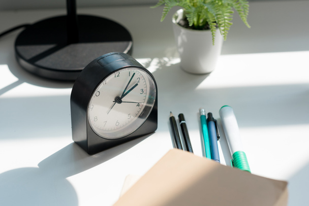 close-up shot of alarm clock with book and pens on workplace - 写真・画像