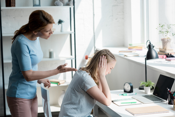 depressed teen daughter sitting at work desk at home while her mother yelling at her - Photo, Image