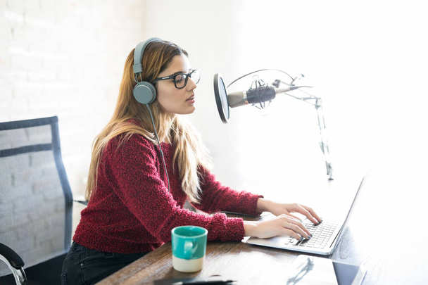 Мила молода жінка з навушниками і ноутбуком розмовляє в мікрофон
 - Фото, зображення
