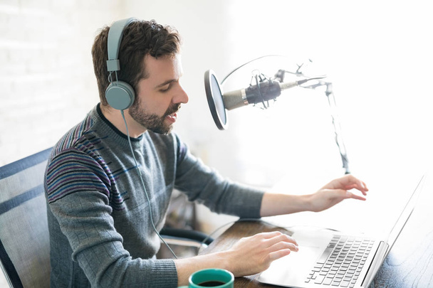 Вид профілю красивого молодого латинського чоловіка, який використовує ноутбук і приймає в мікрофон, розміщуючи онлайн радіо
. - Фото, зображення