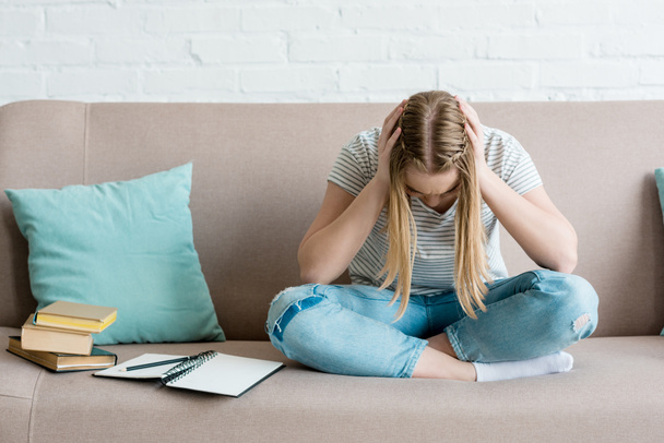 depressed teen girl sitting on couch with books and holding head - Foto, immagini