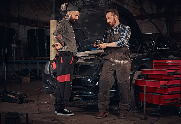 Mluvení během dvou mechanik opravuje rozbité auto v garáži. - Fotografie, Obrázek