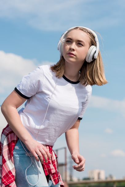 bela menina adolescente em fones de ouvido na frente do céu azul
 - Foto, Imagem