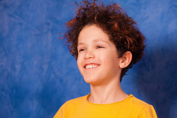 Portrait of preteen curly boy smiling and looking into the distance against background with copy-space - Photo, image