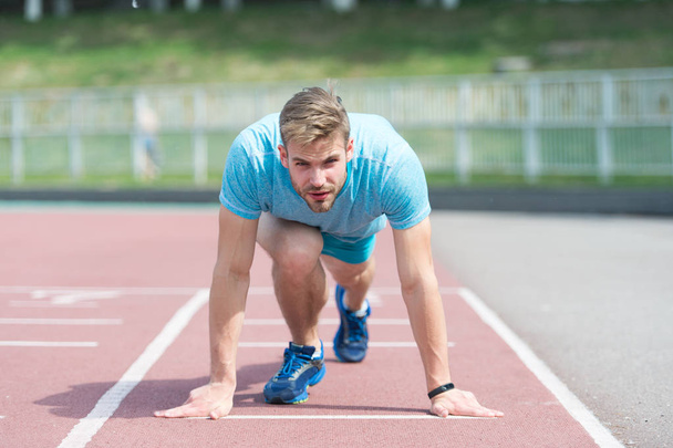 Man runner on start position at stadium. Runner in start pose on running surface. Man run outdoor at running track. Sport and athletics concept. Sportsman on concentrated face ready to go - Foto, imagen