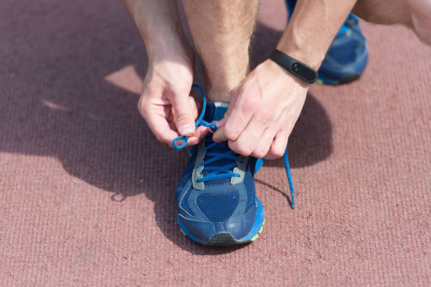 Hands tying shoelaces on sneaker, running surface background. Hands of sportsman with pedometer tying shoelaces on sporty sneaker. Running equipment concept. Shoelaces tying by male hands - Zdjęcie, obraz