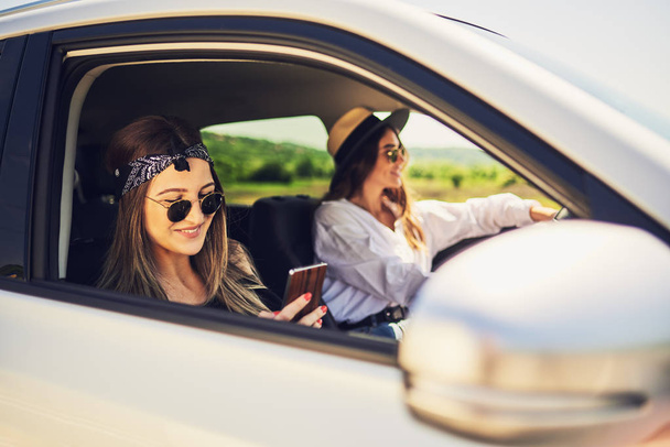 Due ragazze che guidano in macchina. Una ragazza guida e l'altro utilizzando lo smart phone per il messaggio di testo
. - Foto, immagini