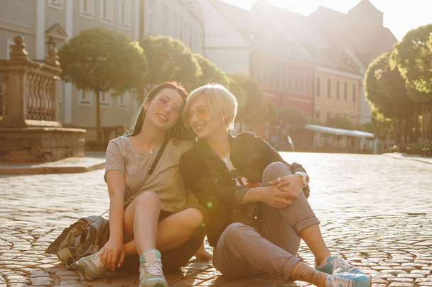 beautiful young women sitting on cobbled street together on sunset - Photo, Image