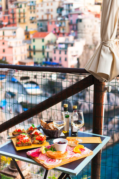 Romantic dinner for two at sunset. White wine and Tasty italian snack: fresh bruschettes  and meat on the board in outdoor cafe with amazing view in Manarola, Italy - Fotografie, Obrázek