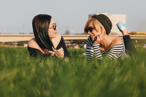 felices mujeres jóvenes tumbadas en la hierba en el parque y charlando
 - Foto, Imagen