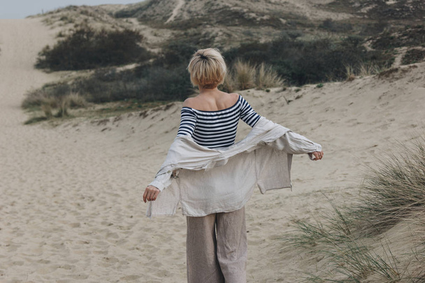 rear view of young woman in stylish clothes on sand dune - Foto, Imagem
