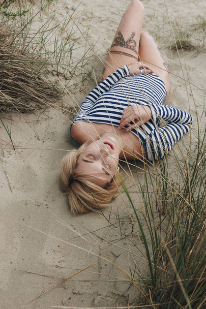 vista de ángulo alto de la sensual mujer joven en traje de cuerpo rayado acostado en la arena
 - Foto, imagen