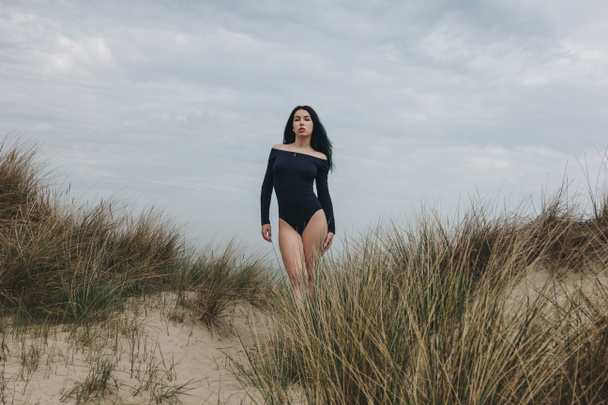 attractive young woman in black bodysuit on sand dune under cloudy sky - Photo, Image