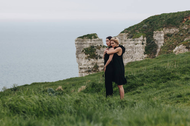 όμορφες νεαρές γυναίκες, αγκαλιάζοντας στον βράχο μπροστά στον ωκεανό, συννεφιασμένη μέρα - Φωτογραφία, εικόνα