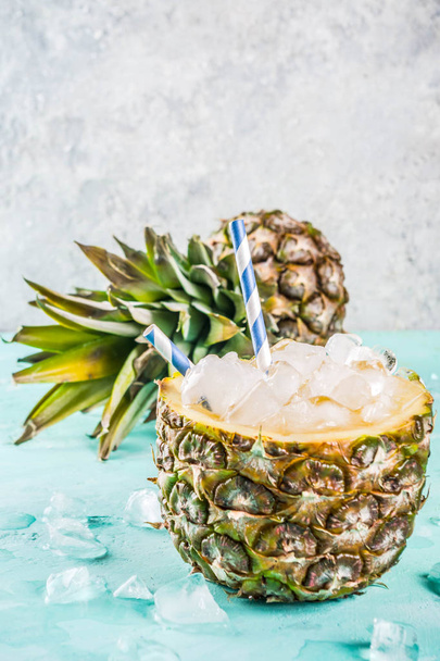 Summer refreshment drink concept, tropical pineapple cocktail or juice in pineapple with ice, light blue concrete background copy space - Foto, afbeelding