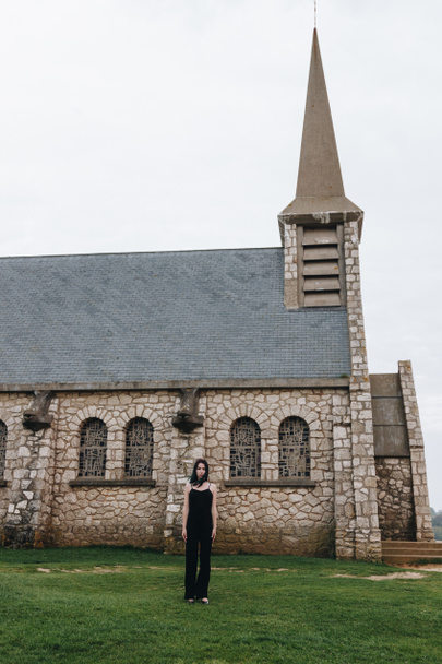 attractive young woman standing on green grass in front of ancient church - Foto, afbeelding
