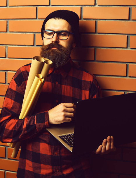 Bearded brutal caucasian hipster holding laptop and craft paper - 写真・画像