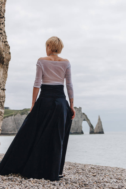rear view of fashionable elegant girl on shore near cliffs and sea, Etretat, Normandy, France - Фото, изображение