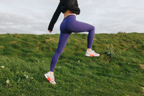 cropped view of athletic woman in stylish sportswear exercising on green grass, Etretat, France - 写真・画像