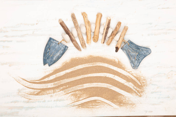Flat lay nautical design with hand-crafted fish of pebbles, stone and wood arcing above a decorative wave of golden beach sand on old vintage style textured white and blue  wood - Valokuva, kuva